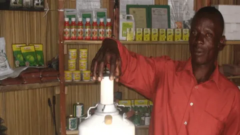 Man demonstrating input-shop equipment inside an agrodealer store stocked with crop-protection products