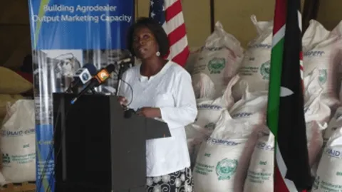 Woman speaking at a podium beside US and Kenya flags at a Purchase for Progress event