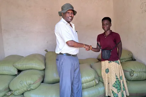 Trader and transporter shaking hands beside sacks of grain near the Malawi-Tanzania border