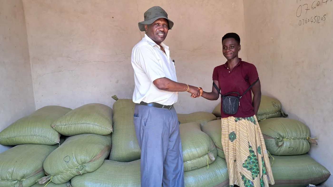 Trader and transporter shaking hands beside sacks of grain near the Malawi-Tanzania border