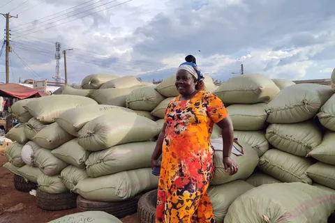 Woman trader standing before a stack of grain sacks at the Busia border market